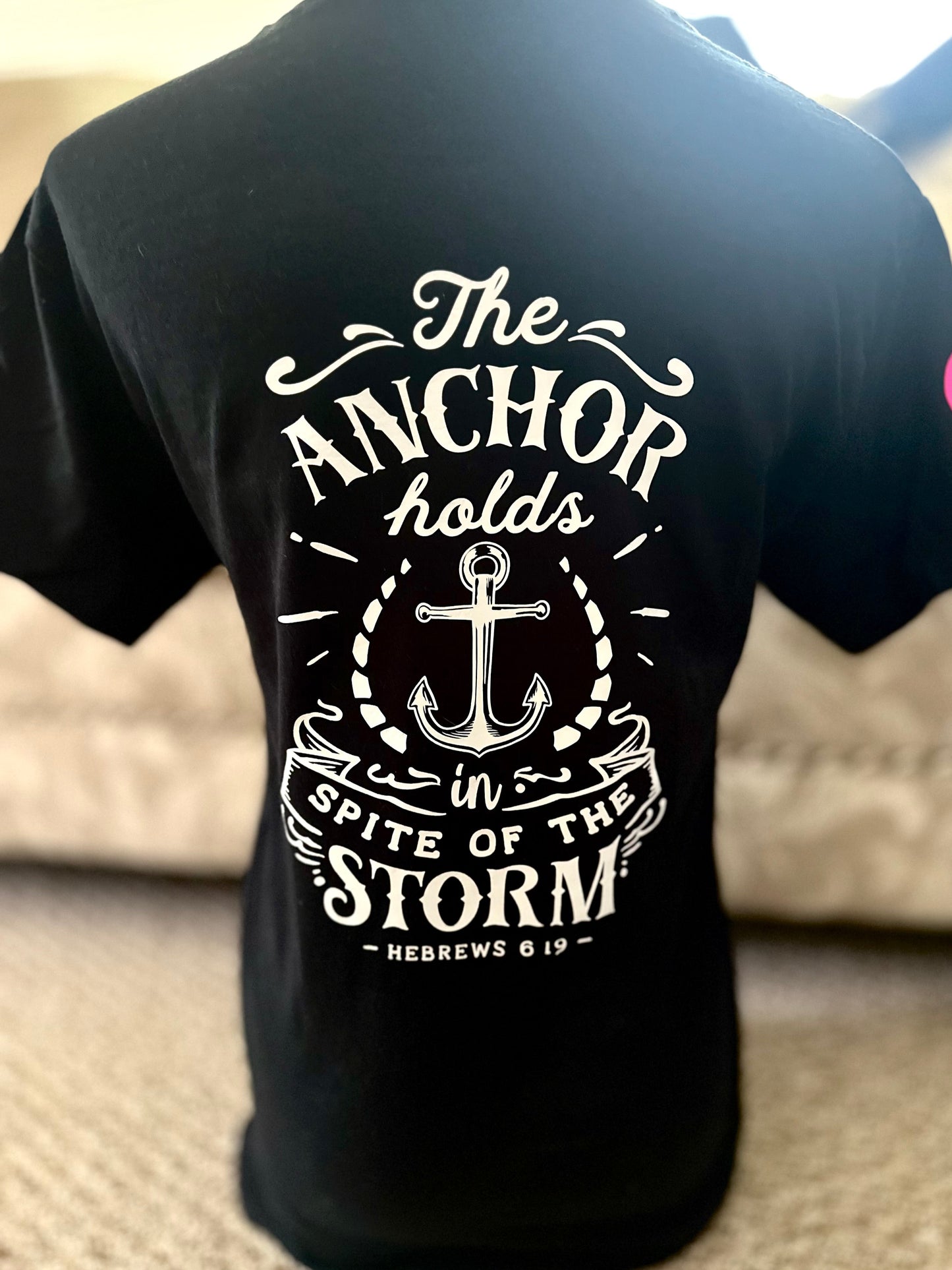 Black t-shirt with white anchor design and text on the back, worn by a person.